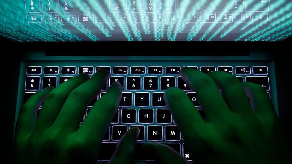 Close up of the hands of a man typing on a computer keyboard. It's very dark, but the keyboard is lit up with data scrolling through the screen