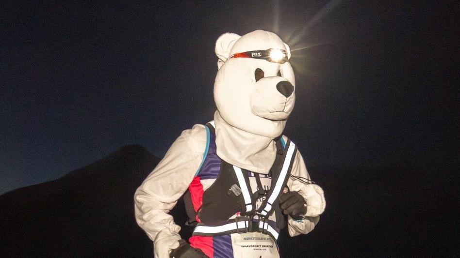 Gill Punt is dressed in a polar bear suit with a head torch on and can be seen running in total darkness at the polar night marathon