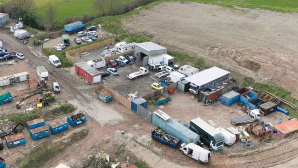 An aerial image of a site at Borstal near Rochester where more than 34,000 cubic metres of waste has been illegally dumped. There are a number of cars, vans and lorries on the site alongside various blue crates.