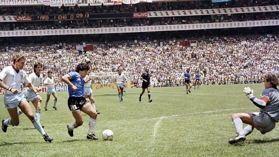 Maradona is seen dribbling the ball through a number of English footballers and the English goalkeeper is seen diving to the side.