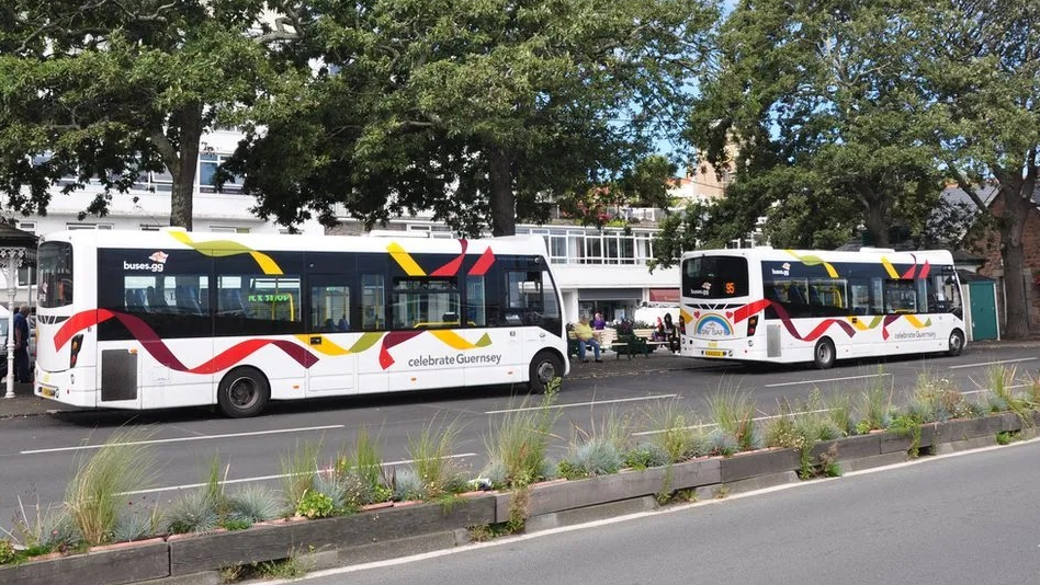 Two white buses with red and yellow livery next to a bus terminus
