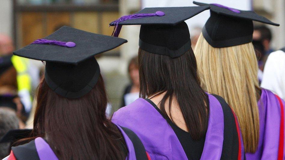 The back of three students wearing red, purple and black cap and gowns. 