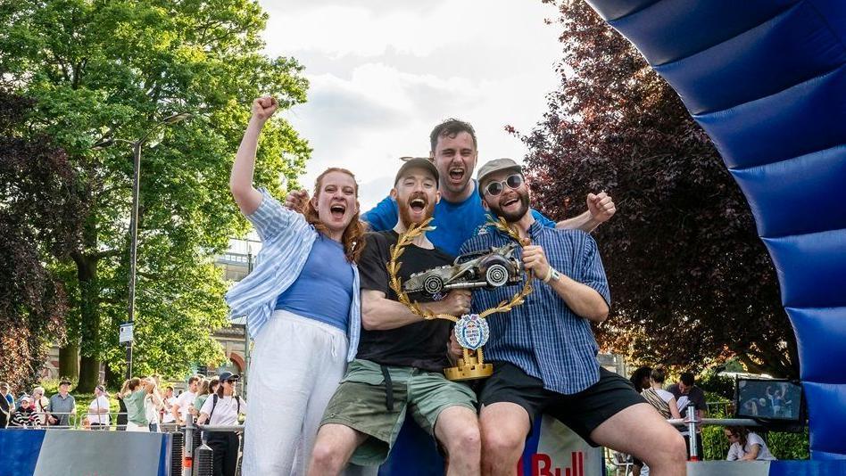 A group of racers holding up a trophy on a podium and cheering