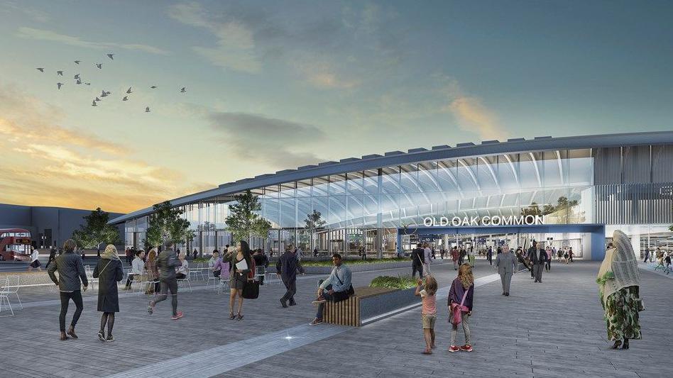 An image shows a large, glass station with a curved roof with passengers in the concourse area