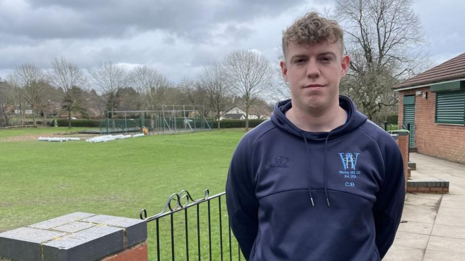 A male cricketer standing in front of a cricket field