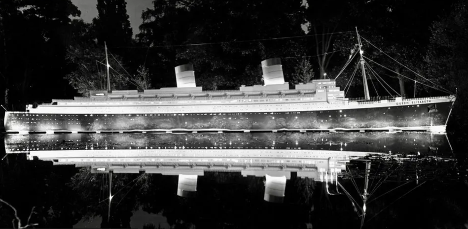 A black and white photo of an ocean liner lit up in the gardens