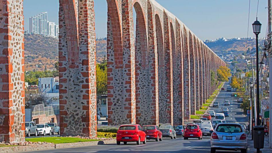 The stone arches of Querétaro's aqueduct run into the distance next to a road
