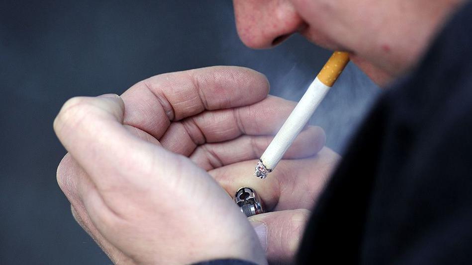 Close-up of a man's hands as he lights a cigarette using a lighter