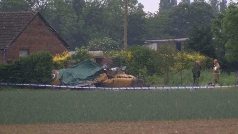 The crashed Spitfire in a field, next to a bungalow, with a green tarpaulin covering the cockpit