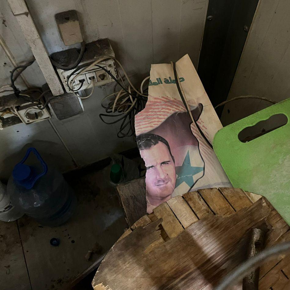 A torn picture of Bashar al-Assad sits among other household items including a chopping board, with electrical wires coming out of a wall nearby