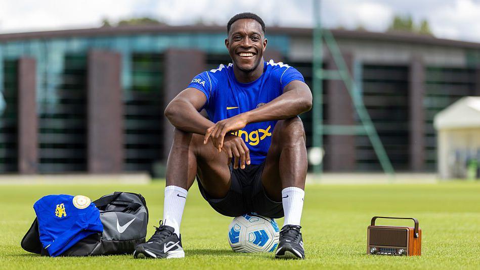Danny Welbeck smiling and sat on a ball