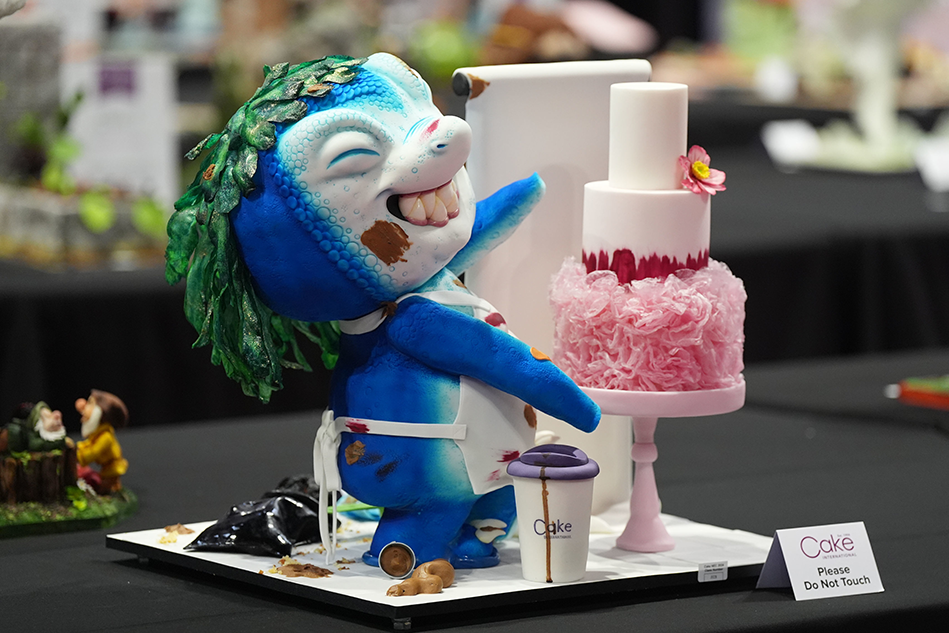 A grinning blue monster presents a miniature cake with a flourish.