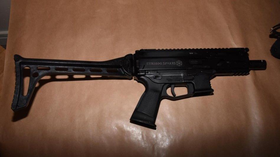 A black gun. It looks menacing and powerful with a large butt on the back to rest against the shoulder.