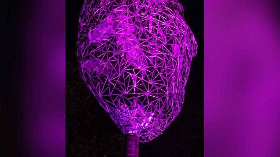 A sphere statue on a pole. Inside the sphere there are feathers and it has been lit up to be purple.