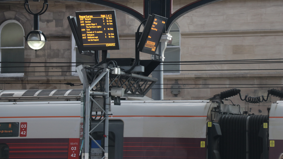 An LNER train sits at a platform at Newcastle Central station. You can also see the departure board. 