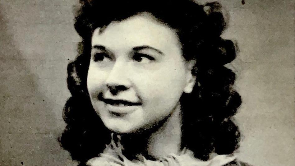 An old black and white photograph of Dorothy Smith wearing a coat and scarf. Her hair is in curls and she is looking off to her right smiling