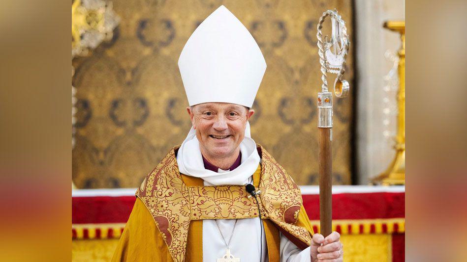 Bishop Mike Harrison smiling at the camera while wearing his Pontifical vestments and standing in front of an alter. 