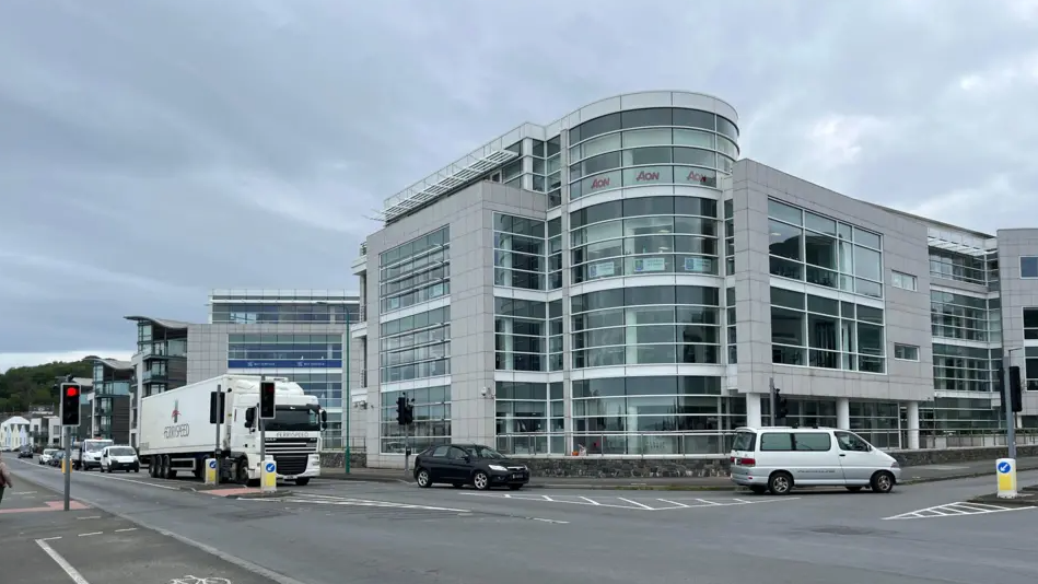 Office buildings housing finance businesses next to a road with cars, vans and lorries on the road.