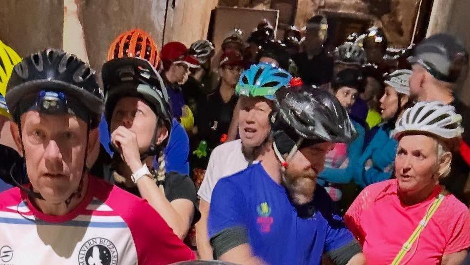 A group of runners in a tunnel, all wearing colourful running gear along with cycle helmets and torches