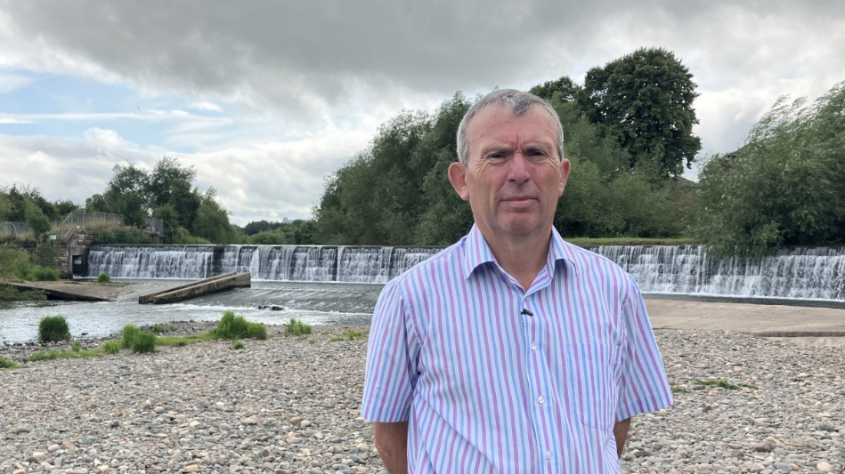 Mr Eckersley wears a striped shirt and is standing in front of floodgates