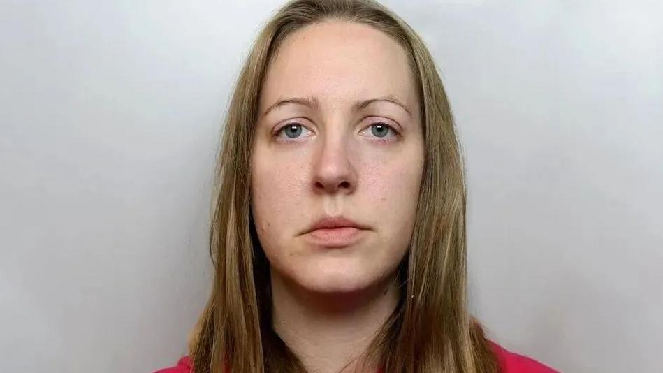 A mug shot of Lucy Letby, She is wearing a red top and wears her dark blonde hair down as she looks into the camera.