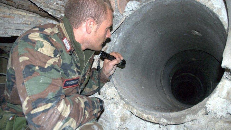 Carabinieri officer peers into tunnel leading to a mafia bunker