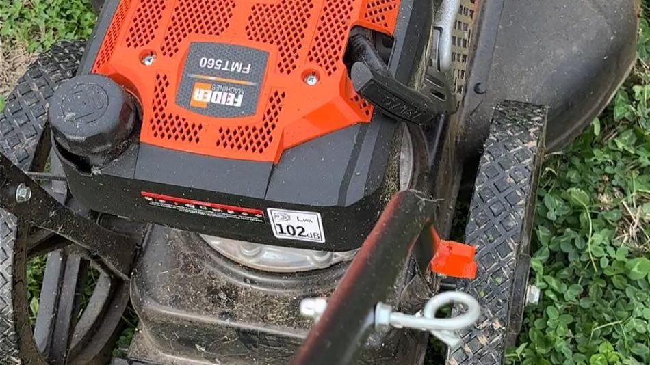 A close-up of an orange and black mower, showing the wheels and the motor. A logo on the mower includes the name "Feider Machines".