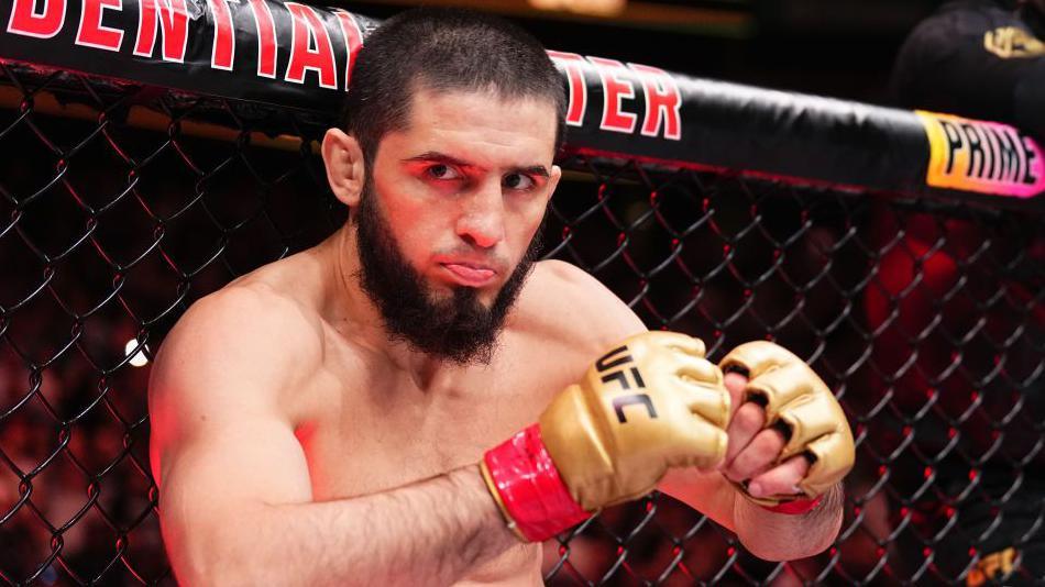 Islam Makhachev sticks out his tongue leaning against the UFC octagon as he prepares to fight