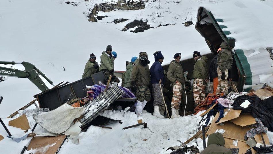 Rescue workers standing by the wreckage of a metal container that was swept down by a snow avalanche on a mountain in Uttarakhand