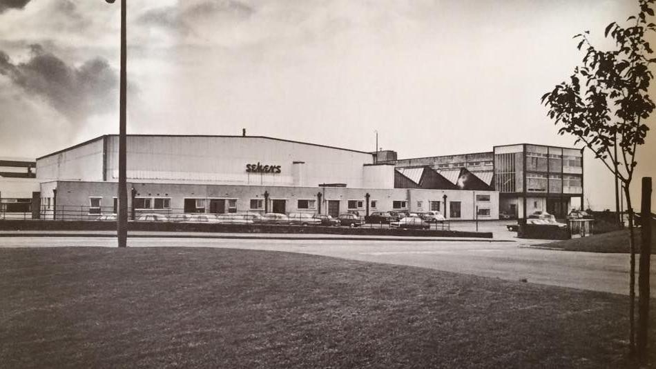 A black and white image of a factory in the 1970s with the words Sekers on the wall.