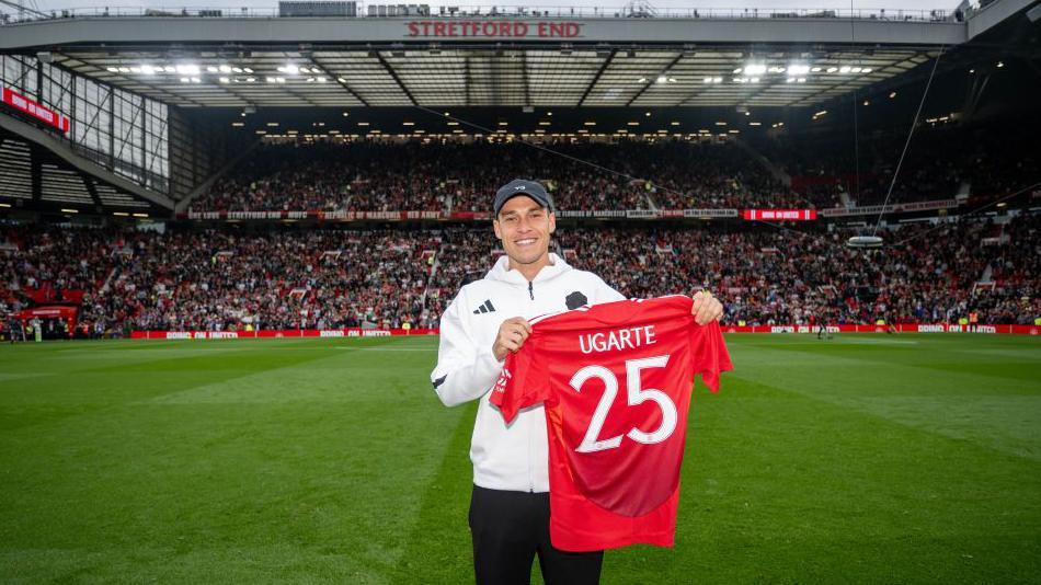 Manuel Ugarte holds up a Manchester United shirt on the pitch at Old Trafford