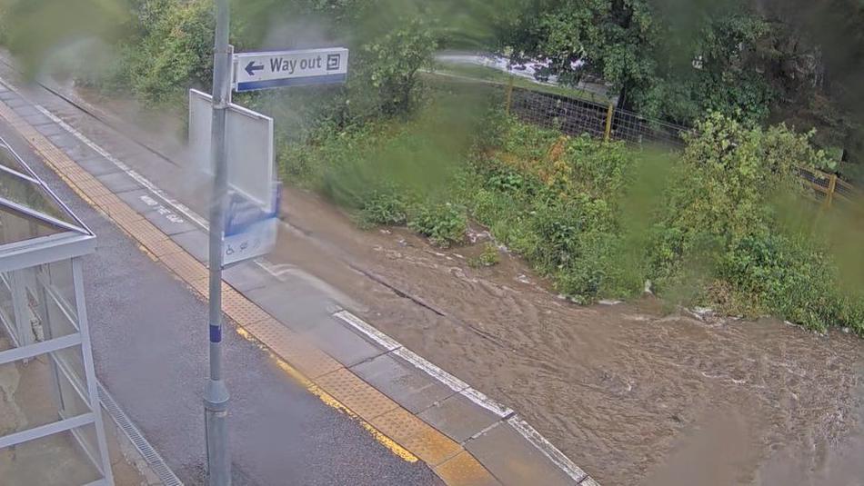 CCTV image of Achanalt station showing muddy water flowing down the railway line reaching almost as high as the platform.