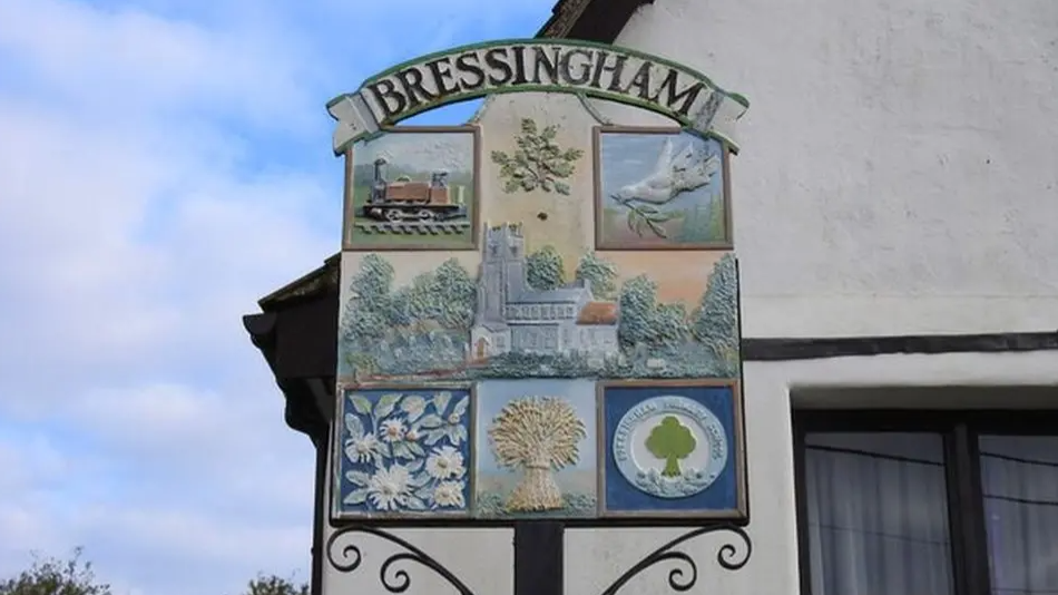 village sign for Bressingham in Norfolk showing wheatsheafs, doves, trains and a church in the centre