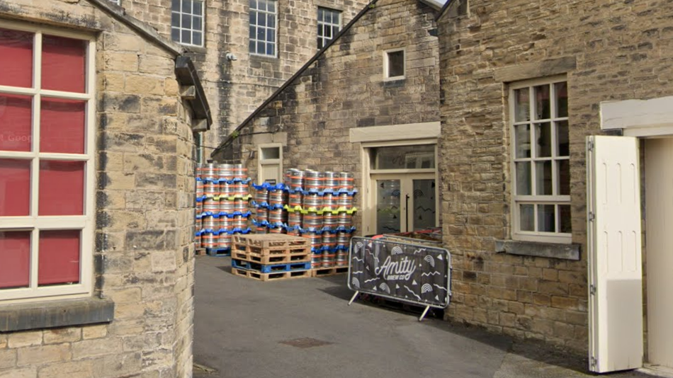 Metal barrels and a fence sign reading Amity outside some mill buildings.