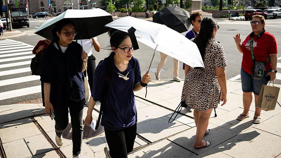 Pedestrians carry umbrellas to shield themselves from the sun during high temperatures in Washington, DC