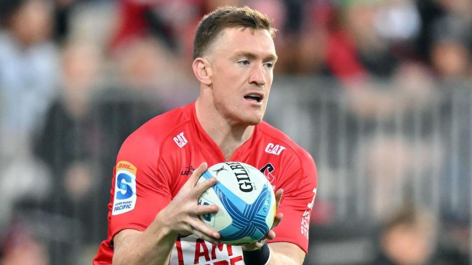 Dallas McLeod holds the ball in two hands in front of him while on the pitch during a match for Crusaders
