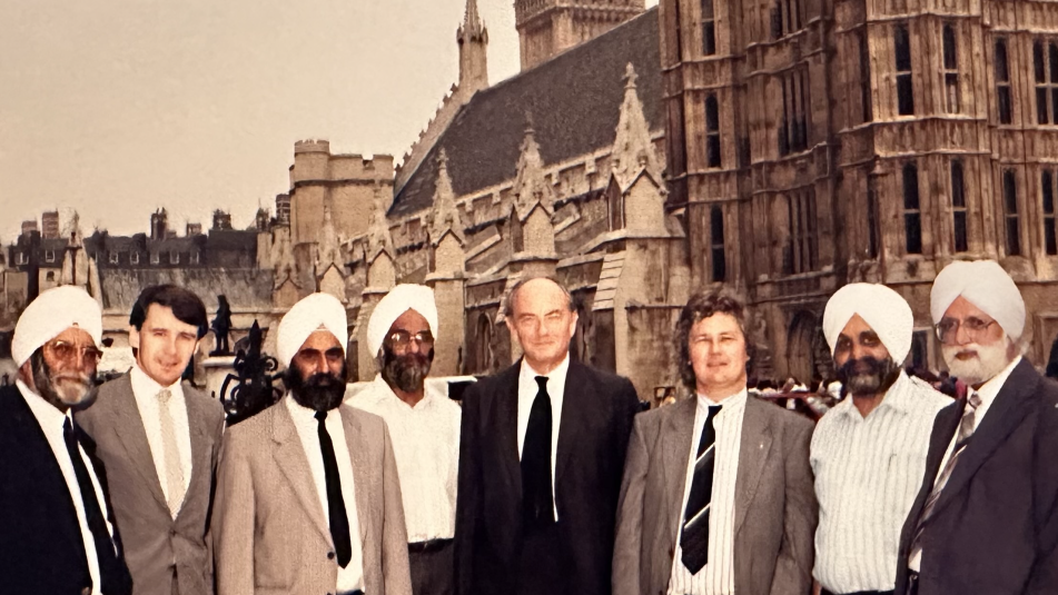 A group of eight men, five of them wearing turbans, outside the Houses of Parliament. Sepia photograph.