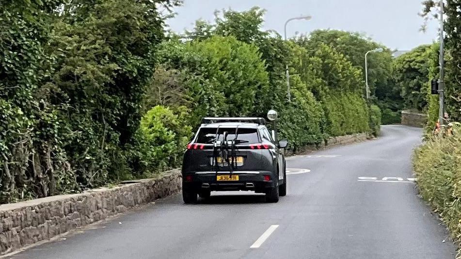 Route de Noirmont. A narrow road with trees and bushes either side. The picture shows the white lines running along the road until they stop and don't go any further.