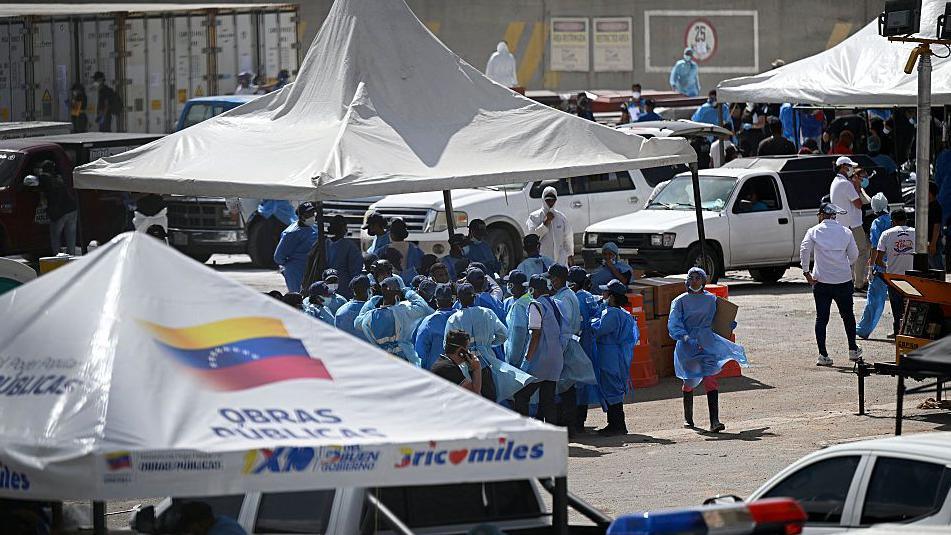 A group of staff officers in blue protective wear stand beneath a white tent