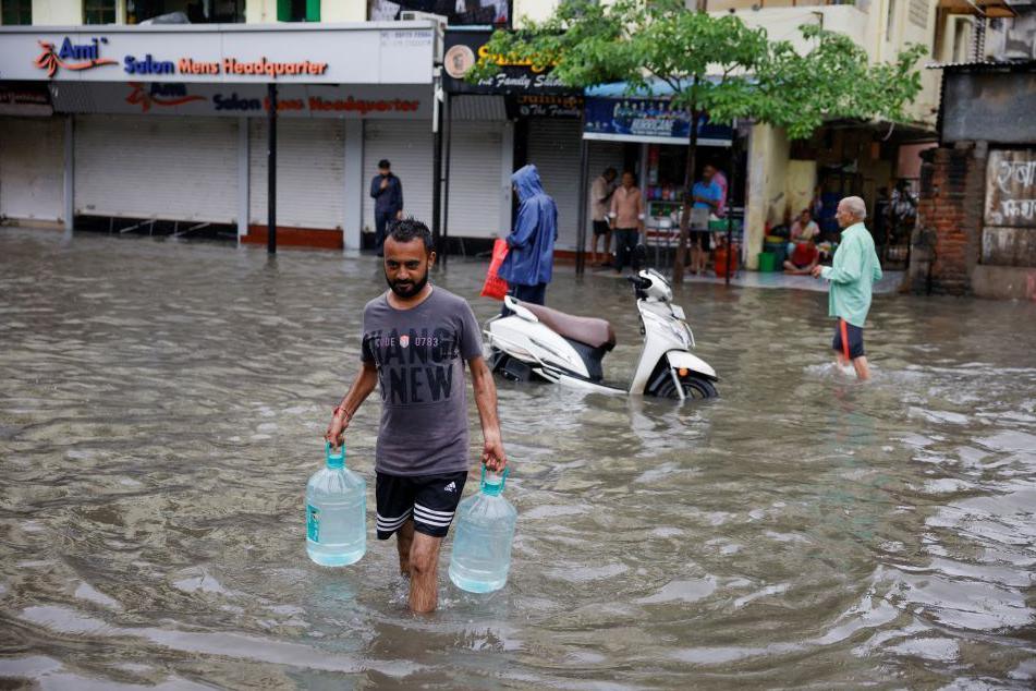  A man carries drinking water across a flooded street, following heavy rains, in Ahmedabad, India, August 27, 2024