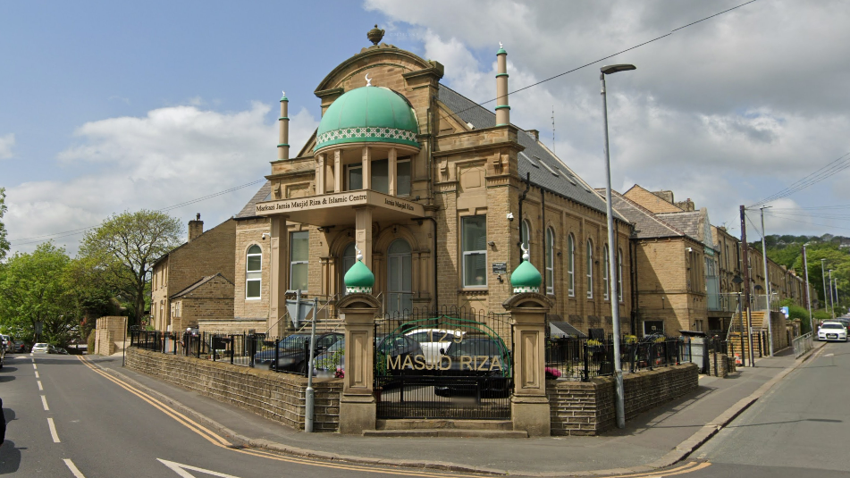 A mosque. It is a grand sandstone building with circular turquoise domes on top of two columns outside, and one dome over the entrance to the building.