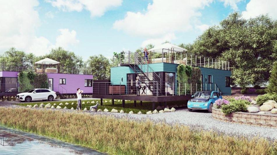 Artist's impression of the proposed site, with a river in the foreground, and  purple and blue-coloured lodges 