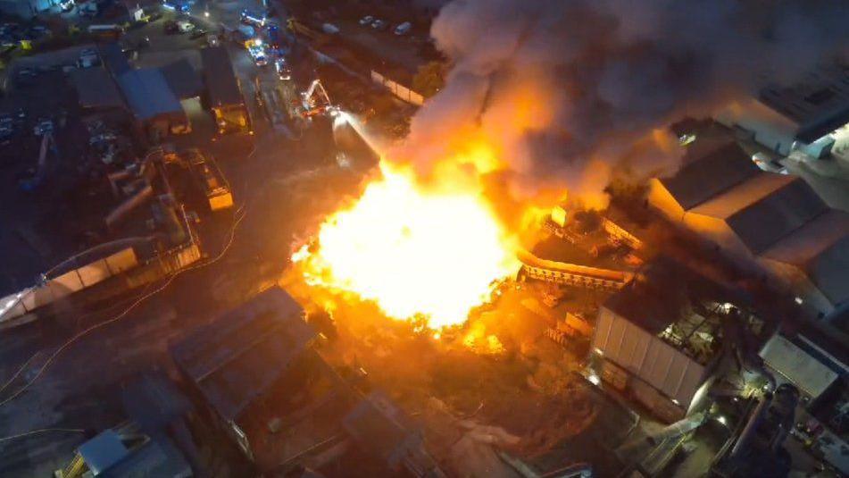 Ariel view of a huge fire, which looks like a glowing yellow ball, in the centre of a recycling centre.