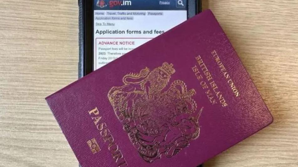 A maroon passport place diagonally over and mobile phone screen that is showing the Manx government webpage for passport application information.