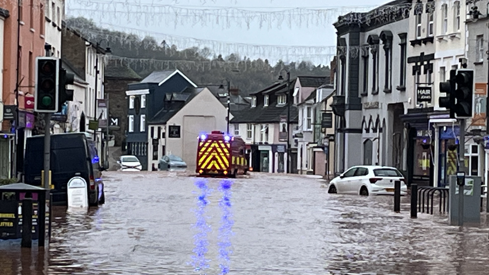 Several cars and an emergency vehicle line the street with water up to their tyres