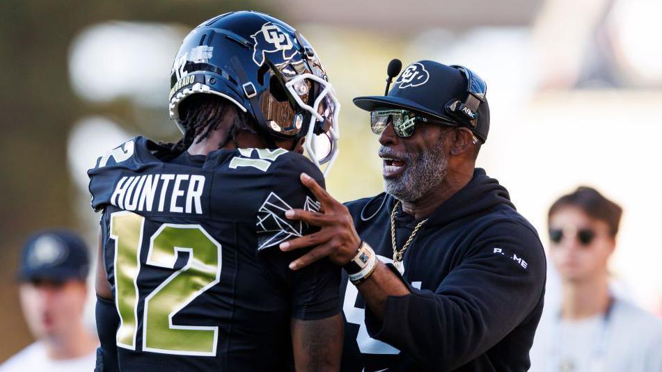 Colorado head coach Deion Sanders talks to Travis Hunter while holding his shoulders on the sideline