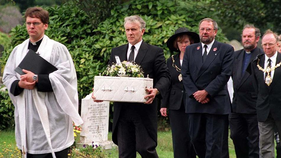 Funeral procession held for the baby showing a priest leading the infant carried in a white coffin by a man in a black suit with other mourners following