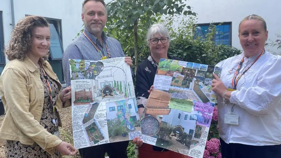 People involved in the project holding big charts displaying the artist's design of the garden, smiling for the camera