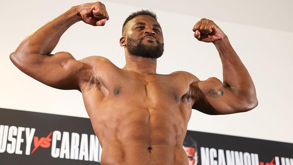 Francis Ngannou flexes and smiles while weighing in