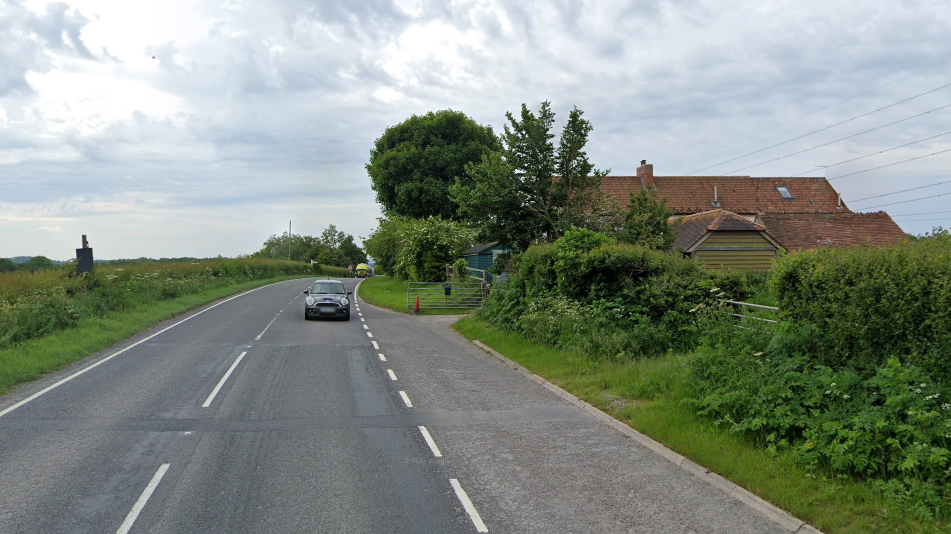 View down Hinkley Point Road, with a terracotta-roofed house with a gate to the right and a low hedge to the left.